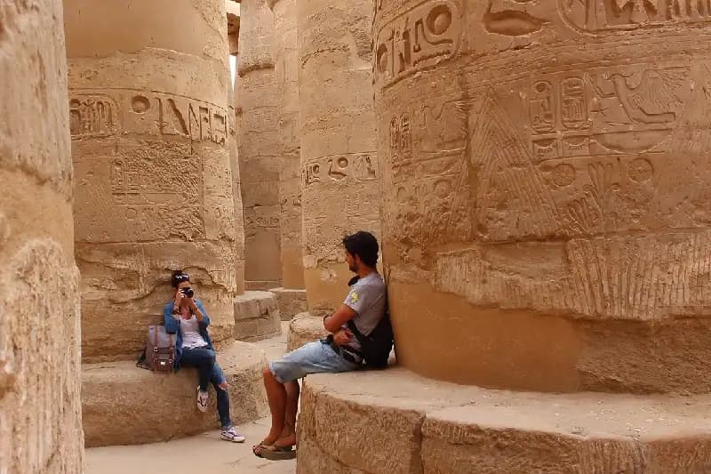 Consejos para Evitar Multitudes en los Templos Egipcios Pareja joven tomándose fotografías entre las columnas de la sala hipóstila del templo de Karnak en Luxor, Egipto.