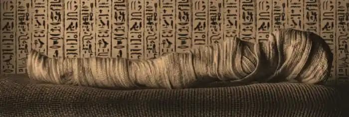 Momia del Antiguo Egipto Momia egipcia frente a un muro con jeroglíficos.