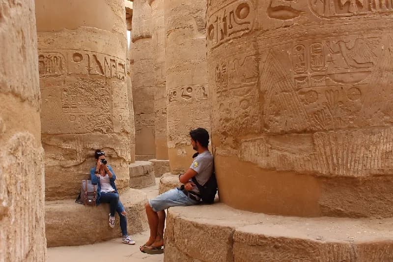 Consejos para Evitar Multitudes en los Templos Egipcios Pareja joven tomándose fotografías entre las columnas de la sala hipóstila del templo de Karnak en Luxor, Egipto.